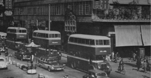 An old photograph of the Daimaru department store in Hong Kong taken across a busy street filled with buses, cars, and pedestrians.