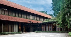The entrance to a red brick building, the Yokohama Cosmetic Education Center, surrounded by trees and shrubbery.