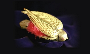 An antique compact cosmetics case, “Bird in Hand”, in the shape of a gold bird with one wing open revealing a red, fluffy material underneath.