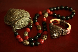 An heirloom of Nepalese King Birendra: a carved silver and bone bracelet of multi-colored beads with a small, gold compact attached, next to a ring.