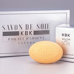 Three silver-colored packages with a bar of soap in front from the SAVON DE SOIE silk soap product line launched in the 1930s.