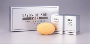 Three silver-colored packages with a bar of soap in front from the SAVON DE SOIE silk soap product line launched in the 1930s.