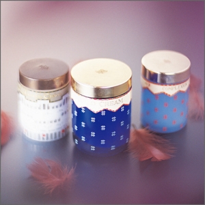 Three product containers featuring unique textile patterns positioned side-by-side surrounded by three feathers.