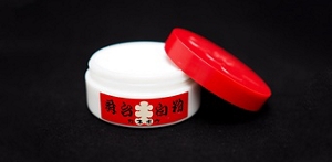 Round, white, and red Kabuki foundation case. On its side rests the open lid revealing the white makeup contained inside.