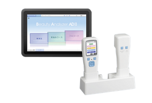 Two white technological devices in a stand in the foreground with a tablet in the background that reads, “Beauty Analyzer ADII”.