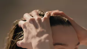 Close-up of a woman running her fingers through her hair, hands on scalp, warm light