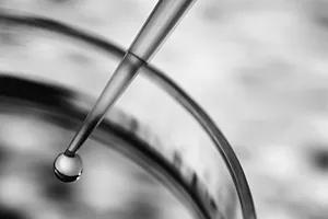 Close-up image of a dropper releasing a droplet of liquid into a container.