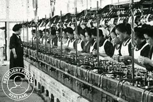 Mange arbeidere står på rekke og spinner silketråd på en fabrikk.