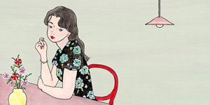 テーブルで物思いにふける、花柄の服を着た黒髪の女性