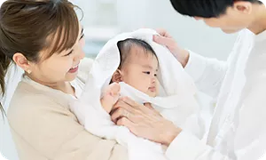 沐浴後に赤ちゃんをやさしくバスタオルで拭くママとパパ