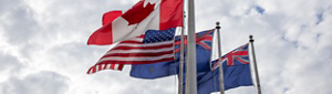 The Canadian, United States, Australian and New Zealand flags blowing in the wind on a cloudy day.