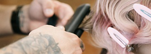 A close-up of hands holding a hair straightener, styling soft pink hair.