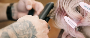 A close-up of hands holding a hair straightener, styling soft pink hair.