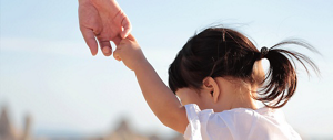 A little girl reaching up holding someone's hand seen from behind
