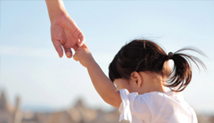 A little girl reaching up holding someone's hand seen from behind