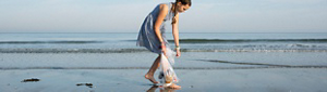 A young teenage girl picking up trash on a beach.