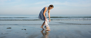 A young teenage girl picking up trash on a beach.