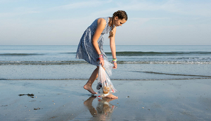 A young teenage girl picking up trash on a beach.