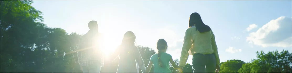 Four people, seen from behind, walk hand in hand across a green field toward the sunlight, symbolizing a bright future for people and the planet