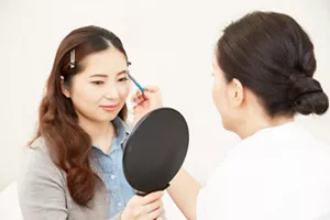 Image of staff applying makeup while explaining to a patient holding a mirror