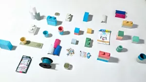 使用済みつめかえパック由来のリサイクル材を配合した、様々な試作品や製品の写真。レンガサイズのカラフルなブロック、植木鉢、3Dプリンターのフィラメントなどが配置されている。