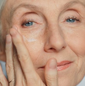 Mature woman with radiant skin patting eye cream around her outer eye area