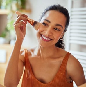 Smiling woman applying make-up to cleansed, moisturised skin