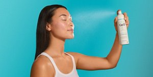 Woman holding a can of moisturising spray against a teal background