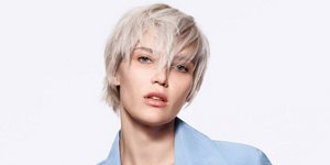 Mujer de aspecto serio con cabello rubio corto y fondo brillante