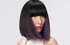 A woman with straight black hair with midnight berry highlights used goldwell elumen creative services in front of a grey background.