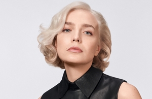 A woman with wavy midnight blonde hair used goldwell elumen blonde toning with elumen colds and elumen warms in front of grey background.