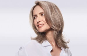 Woman with grey hair smiling and glancing at her right on a shaded grey background