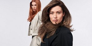 Two women with brown and red hair, using products from the Goldwell Muted Collection, standing in front of a grey background.