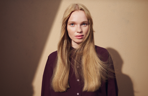 A woman with straight nouveau copper-colored hair, dyed with Goldwell Topchic, standing in front of a grey background.