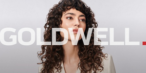 a woman with brown curly hair used goldwell texture dimensions perm product line on a grey background