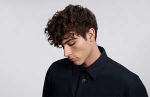a man with brown curly hair used goldwell texture dimensions perm product line on a grey background