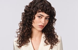 a woman with brown straight hair used goldwell structure and shine products on a grey background looking into the camera