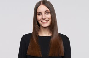 a woman with brown straight hair used goldwell structure and shine products on a grey background looking into the camera