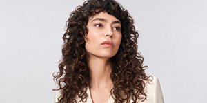 žena sa smeđom kovrdžavom kosom koristila je liniju proizvoda goldwell texture dimensions perm na sivoj pozadini gledajući u kameru