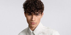 a woman with brown curly hair used goldwell texture dimensions perm product line on a grey background looking into the camera