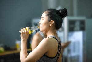 Woman drinking water in her gym clothes with black hair in a gym bun
