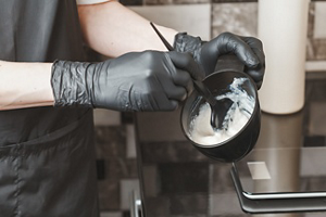 Stylist wearing gloves mixing hair dye in a plastic container