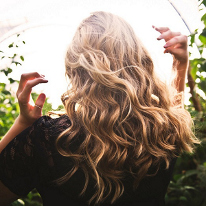 Back of a woman's head reaching for her long, blonde and tousled hair