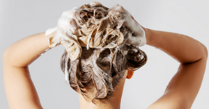 Back of a blonde-haired woman's head while she washes her hair against a white background