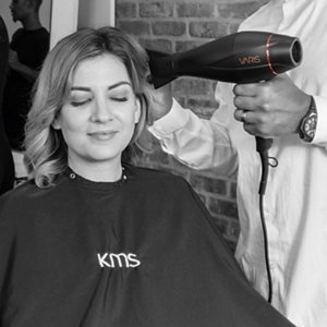 Lächelnder Hairstylist trocknet das Haar einer Frau mit einem Föhn