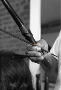 Male hair stylist using VARIS curling iron for styling woman’s hair