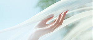 Una mano accarezza un velo bianco semitrasparente sospeso nell’aria.