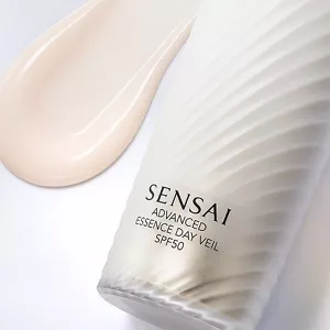 Primo piano di un flacone di Advanced Essence Day Veil con texture a coste diagonali e accanto un campione cremoso di un rosa chiaro