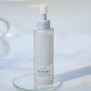 White pump bottle of Silky Purifying Cleansing Gel Water on a glass coaster against a soft blue background