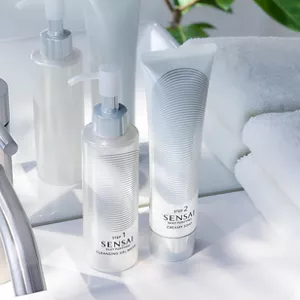 Cleansing Gel Water and Creamy Soap on a white bathroom sink in front of a mirror, with a folded white towel beside them